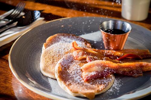 a plate with pancakes and bacon and a cup of syrup at Bartley Lodge Hotel in Lyndhurst