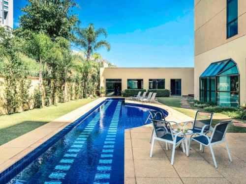a swimming pool with two chairs next to a house at Caesar Business Belo Horizonte Belvedere in Belo Horizonte