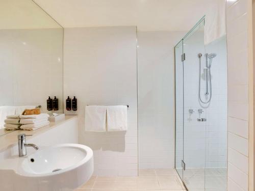 a white bathroom with a sink and a shower at Mercure North Melbourne in Melbourne
