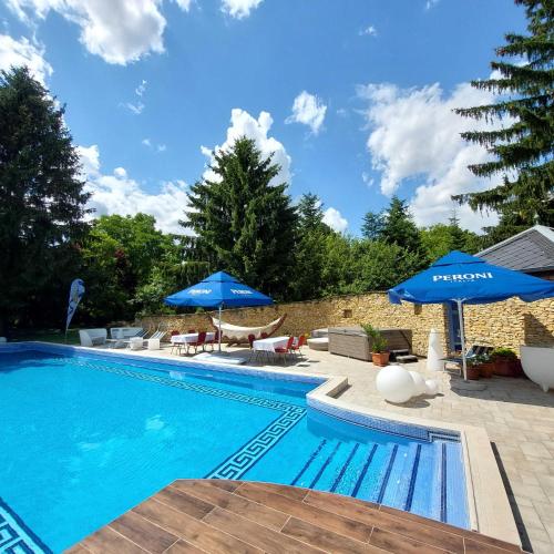 a swimming pool with blue umbrellas and chairs at Castle Garden *** in Szombathely