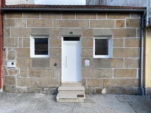 a brick building with a white door and two windows at CASA do CAMPO Lestrove in Padrón