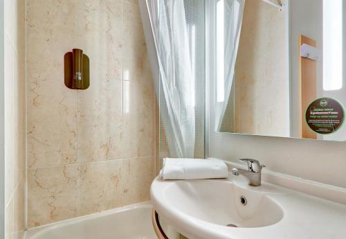 a bathroom with a sink and a mirror and a tub at B&B HOTEL Clermont-Ferrand Le Brézet Aéroport in Clermont-Ferrand