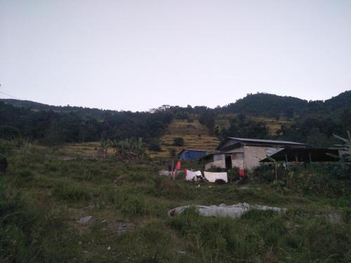 a small house in a field with mountains in the background at Pame Farm Stay in Pokhara