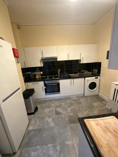 cocina con armarios blancos, lavadora y secadora en Spacious 5-Bed Retreat, en Londres