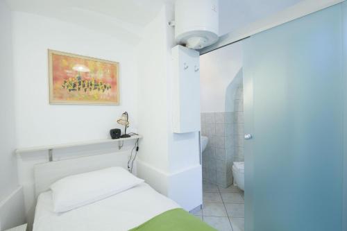 a white bathroom with a bed and a toilet at Tiny central studio apartment Tour As Ljubljana in Ljubljana