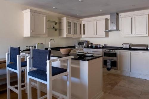a kitchen with white cabinets and a island with blue chairs at South Sands Hotel in Salcombe