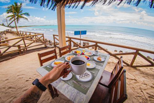 a person sitting at a table with a cup of coffee on the beach at Privê Pontal de Maracaipe in Porto De Galinhas