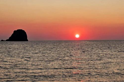 een zonsondergang over de oceaan met een rots in de horizon bij Green Apple in Pollonia