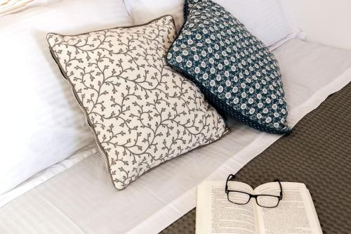 un libro e occhiali su un letto con cuscini di Green Apple a Pollonia