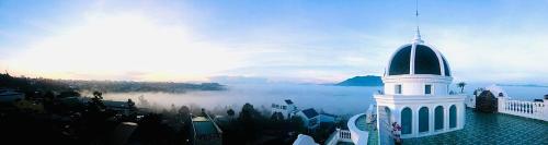 a white building with a black top with a foggy city at Hotel Hoa Nắng in Bao Loc