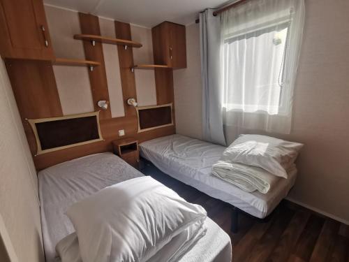 une petite chambre avec deux lits et une fenêtre dans l'établissement Mobil Home proche de la mer, à Saint-Martin-Plage