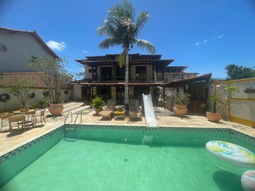 een zwembad voor een huis met een palmboom bij Quarto com banheiro no térreo in Araruama