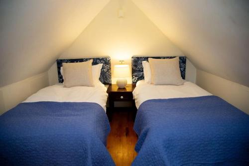 2 letti in una camera mansardata con lenzuola bianche e blu di Bluebell Northbrook Park Chalet a Farnham