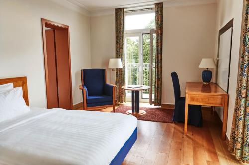 Steigenberger Hotel & Spa Bad Pyrmont في باد بيرمونت: غرفة نوم بسرير ومكتب ونافذة