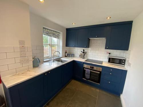 eine Küche mit blauen Schränken, einer Spüle und einer Mikrowelle in der Unterkunft Seahorse Cottage in Helston