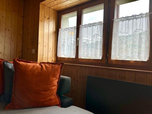Cette chambre dispose de deux fenêtres et d'un canapé avec un oreiller orange. dans l'établissement Les Antilles l Bucolique l 6pers, à Vercorin