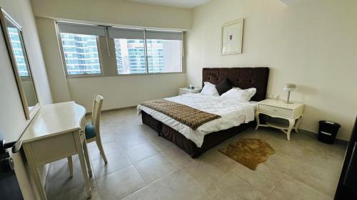 a bedroom with a bed and a desk and two windows at Lakeshore Towers, Cluster Y , JLT, 1BHK in Dubai