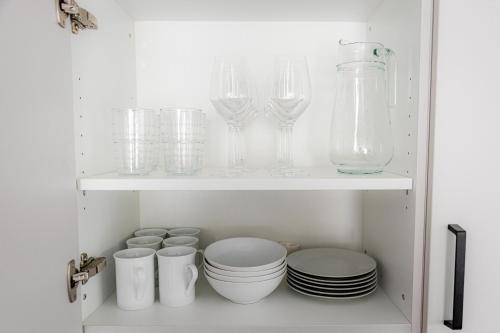 a white cabinet with glasses and plates and bowls at BONNYSTAY Herzogenaurach Natur und Entspannung nähe Zentrum in Herzogenaurach