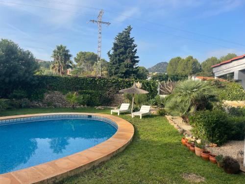 een zwembad in een tuin met een stoel en een parasol bij Nice holiday house with pool at La Sella Golf between Denia and Javea in Pedreguer
