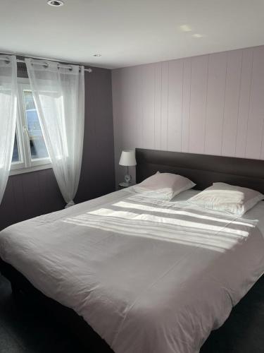 une chambre avec un grand lit blanc avec une fenêtre dans l'établissement Plage du Débarquement. Maison bord de Mer, à Saint-Côme-de-Fresné