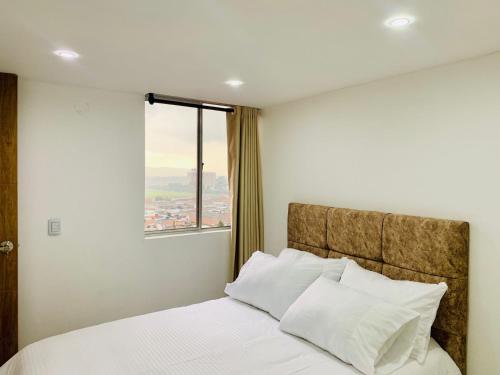 a bedroom with a bed with white sheets and a window at Alquiler Apartamento en Bogotá cerca al aeropuerto-Colibri Dorado in Bogotá