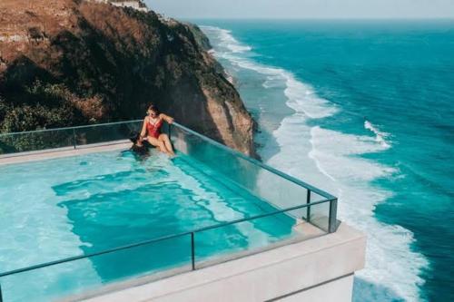 a woman sitting in a swimming pool next to the ocean at glamping camping kamping in Ungasan