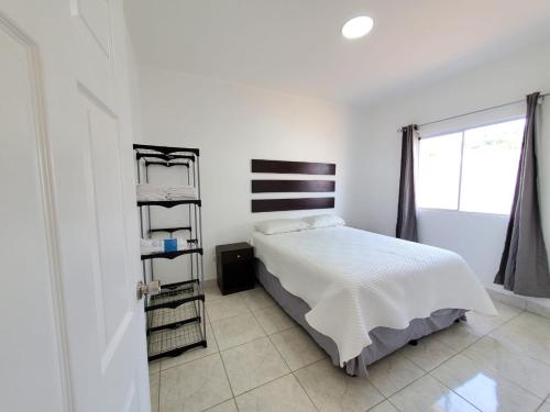 Casa Perla ¡Clima y Comfort! في El Rosario: غرفة نوم بيضاء مع سرير ورف كتاب