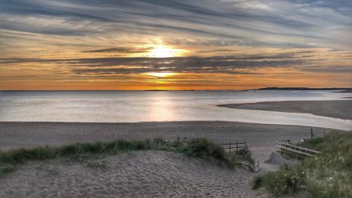 a sunset on a beach with the sun setting over the water at Little Sandy House, Rhosneigr in Rhosneigr