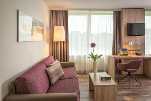 a living room with a couch and a desk in a hotel room at Essential by Dorint Basel City in Basel