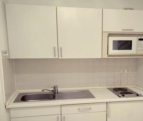 eine Küche mit weißen Schränken, einer Spüle und einer Mikrowelle in der Unterkunft Departamento con dos habitaciones in Santiago