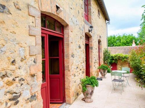 une porte rouge sur un bâtiment en pierre avec une table dans l'établissement Charme et authenticité : gîte pour 4 pers. en bord de rivière avec jardin enchanteur en Sarthe - FR-1-410-236, à Asnières-sur-Vègre