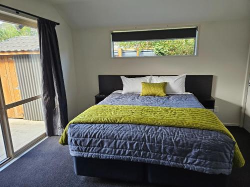 a bedroom with a bed with a yellow blanket and a window at Aachen Place Motel in Greymouth