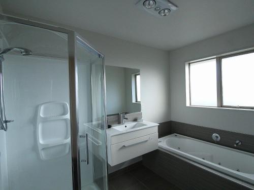 a bathroom with a shower and a sink and a tub at Aachen Place Motel in Greymouth