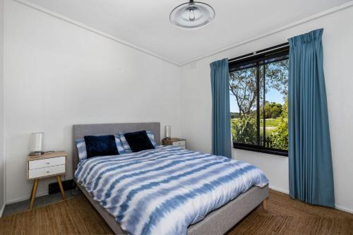 una camera da letto con un letto con tende blu e una finestra di Inverloch' s Lime Green Door - Linen, Wifi, Pet Friendly a Inverloch