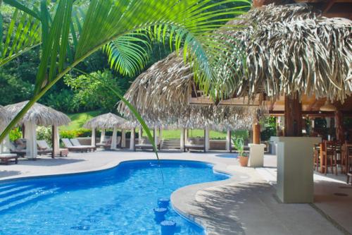 uma piscina de resort com um guarda-sol de palha e cadeiras em Hotel Playa Espadilla & Gardens em Manuel Antonio