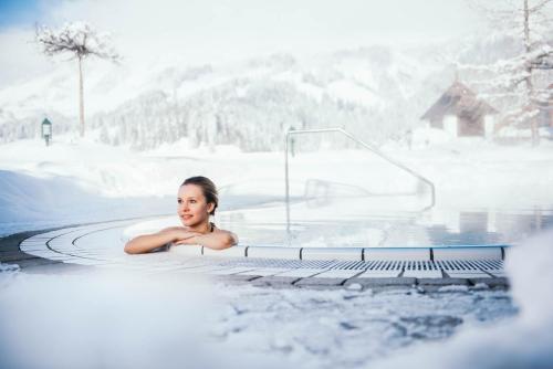 Una mujer tumbada en un jacuzzi en la nieve en Übergossene Alm Resort en Dienten am Hochkönig