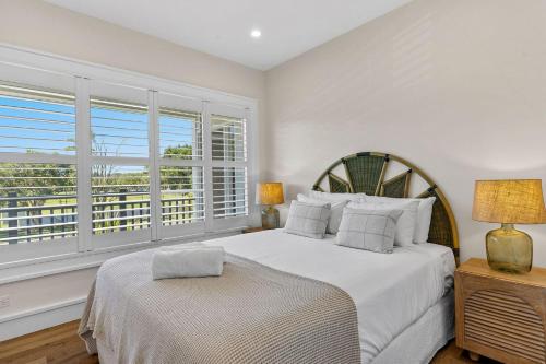 a white bedroom with a bed and a window at Orana Byron in Byron Bay