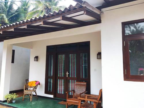 a home with a porch with chairs and a door at Palm Beach Cabana in Kosgoda