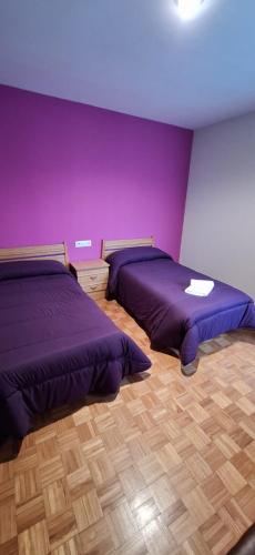 two beds in a room with purple walls and wooden floors at Pensión Río Cenza in Villarino de Conso