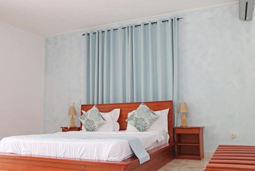 a bedroom with a bed with white sheets and blue curtains at Ocean Blue Bay in Anse Volbert Village
