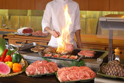 a man cooking meat on a grill with fire at Wellness Forest Ito - Kyoritsu Resort in Ito
