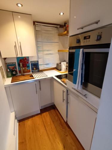 a kitchen with white cabinets and a wooden floor at Little Oak - Double (Kingsize) Self Contained Oak Studio - Sleeps 2 in Chiddingfold