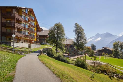 a path in front of a building with mountains in the background at Reka-Feriendorf Hasliberg in Hasliberg