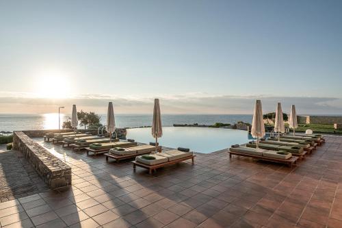 a swimming pool with lounge chairs and umbrellas at Kakkos Beach Hotel - Adults Only in Ierápetra