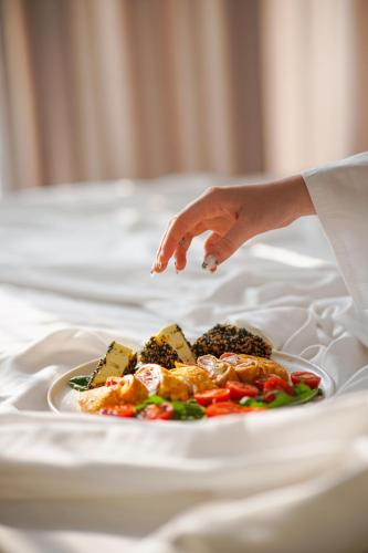 a person reaching for a plate of food on a bed at Royal G Max in Golem