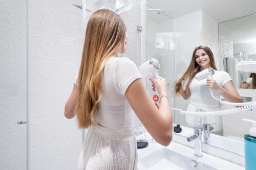 a woman brushing her teeth in front of a mirror at Moov Hotel Lisboa Oriente in Lisbon