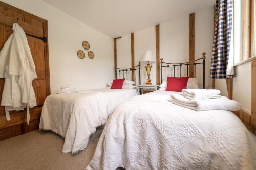 a bedroom with two beds with white sheets and red pillows at Manor Farm Barn in Eye