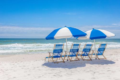 three chairs and two umbrellas on a beach at Hampton Inn & Suites - Orange Beach in Orange Beach
