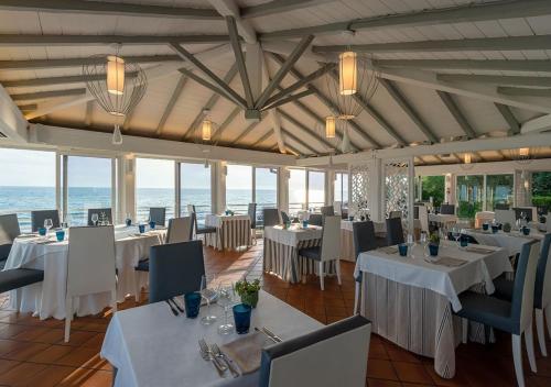 un ristorante con tavoli e sedie bianchi e l'oceano di Hotel Oasi Di Kufra a Sabaudia