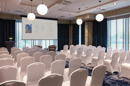 a conference room with white chairs and a projection screen at Arche Hotel Wrocław Airport in Wrocław
